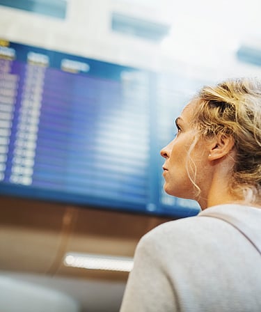 Kvinna som tittar mot avgångstavla på flygplats
