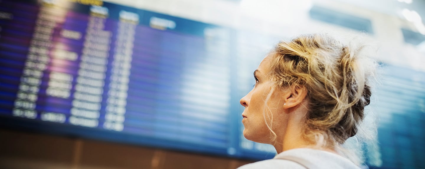 Kvinna som tittar upp mot avgångstavla på en flygplats.