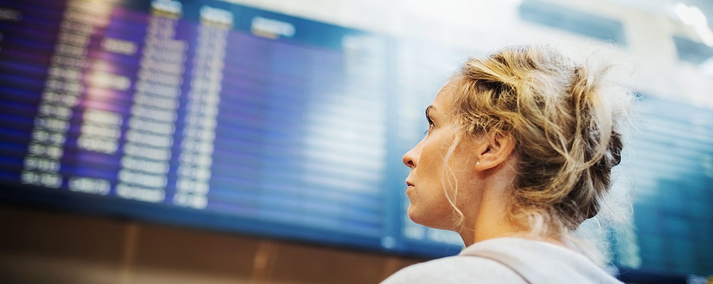 Kvinna som tittar mot avgångstavla på flygplats