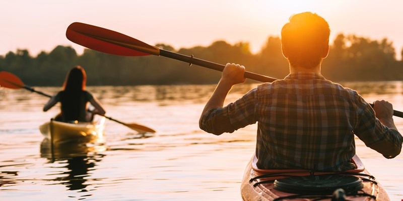 Meeting sunset on kayaks. Rear view of beautiful young couple kayaking on lake together with sunset in the background