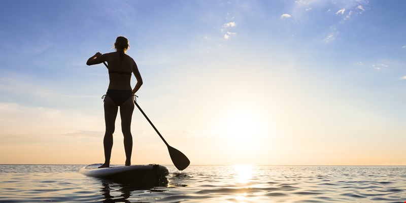 Girl stand up paddle boarding (sup) on quiet sea at sunset