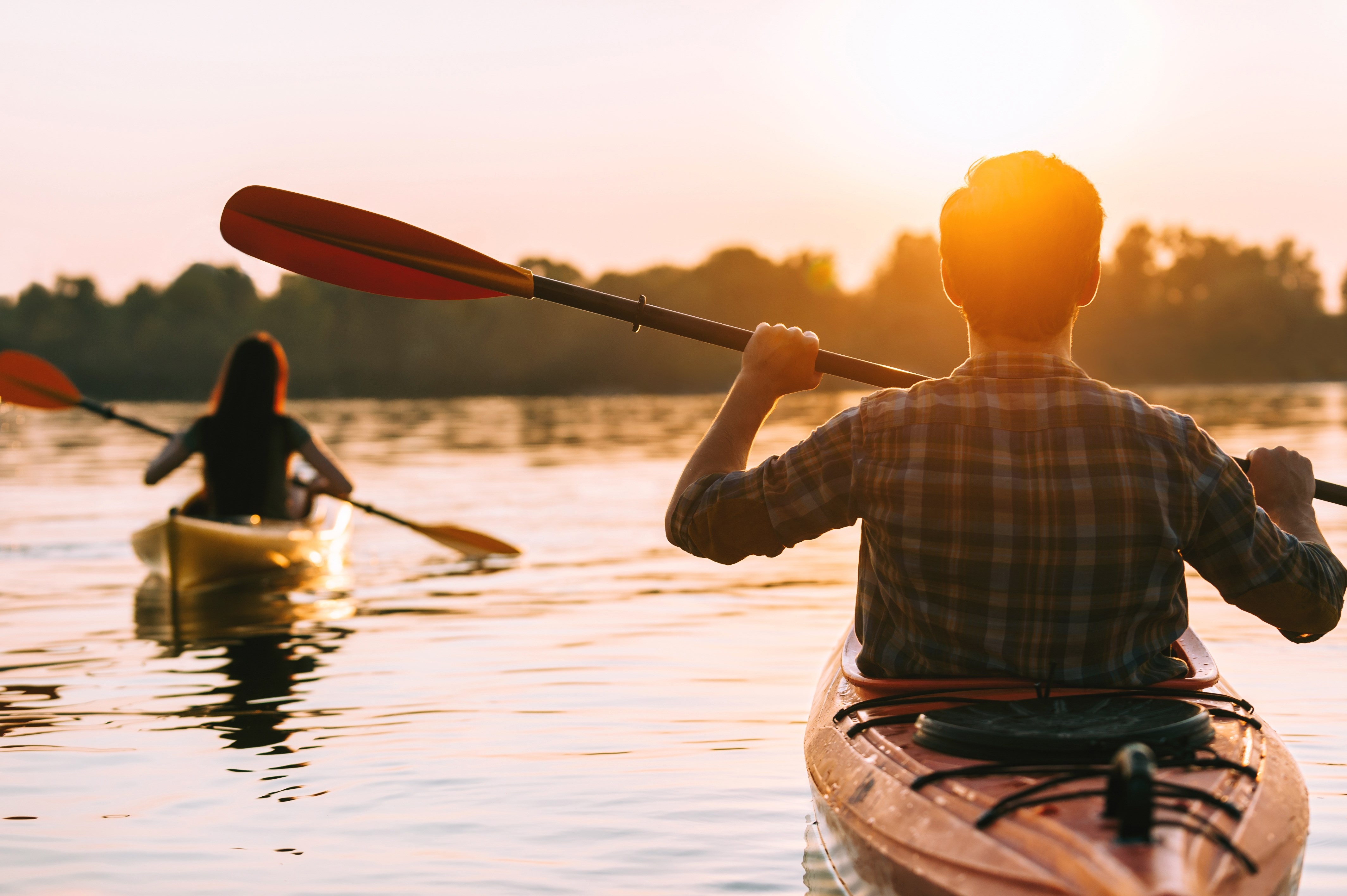 Meeting sunset on kayaks. Rear view of beautiful young couple kayaking on lake together with sunset in the background