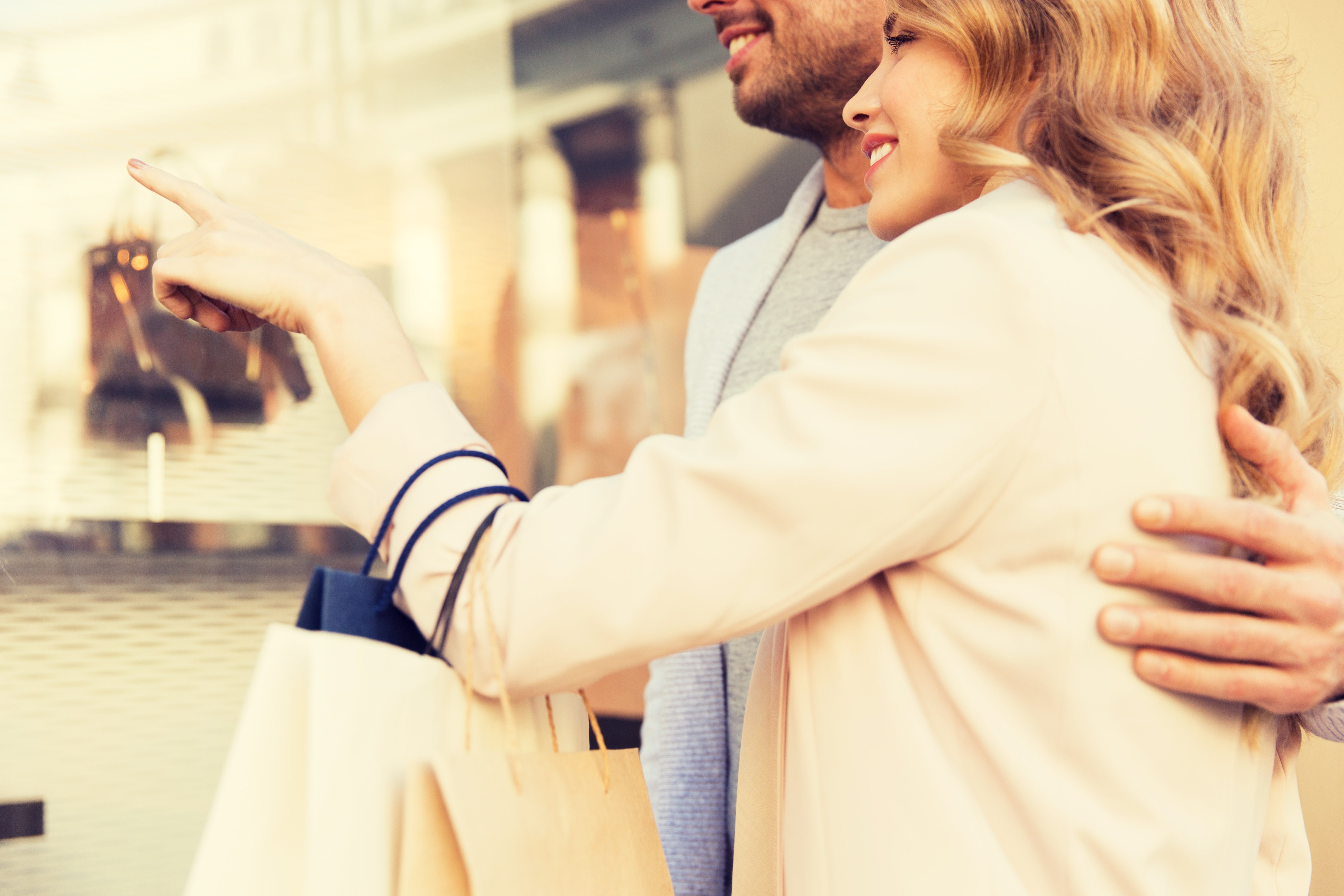sale, consumerism and people concept - close up of happy couple with shopping bags looking at shop window in city