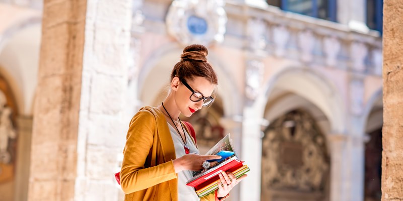 Young female student dressed casually with colorful books in the inner yard of oldest university in the world in Bologna city in Italy