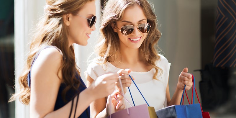 sale, consumerism and people concept - happy young women looking into shopping bags at shop window in city
