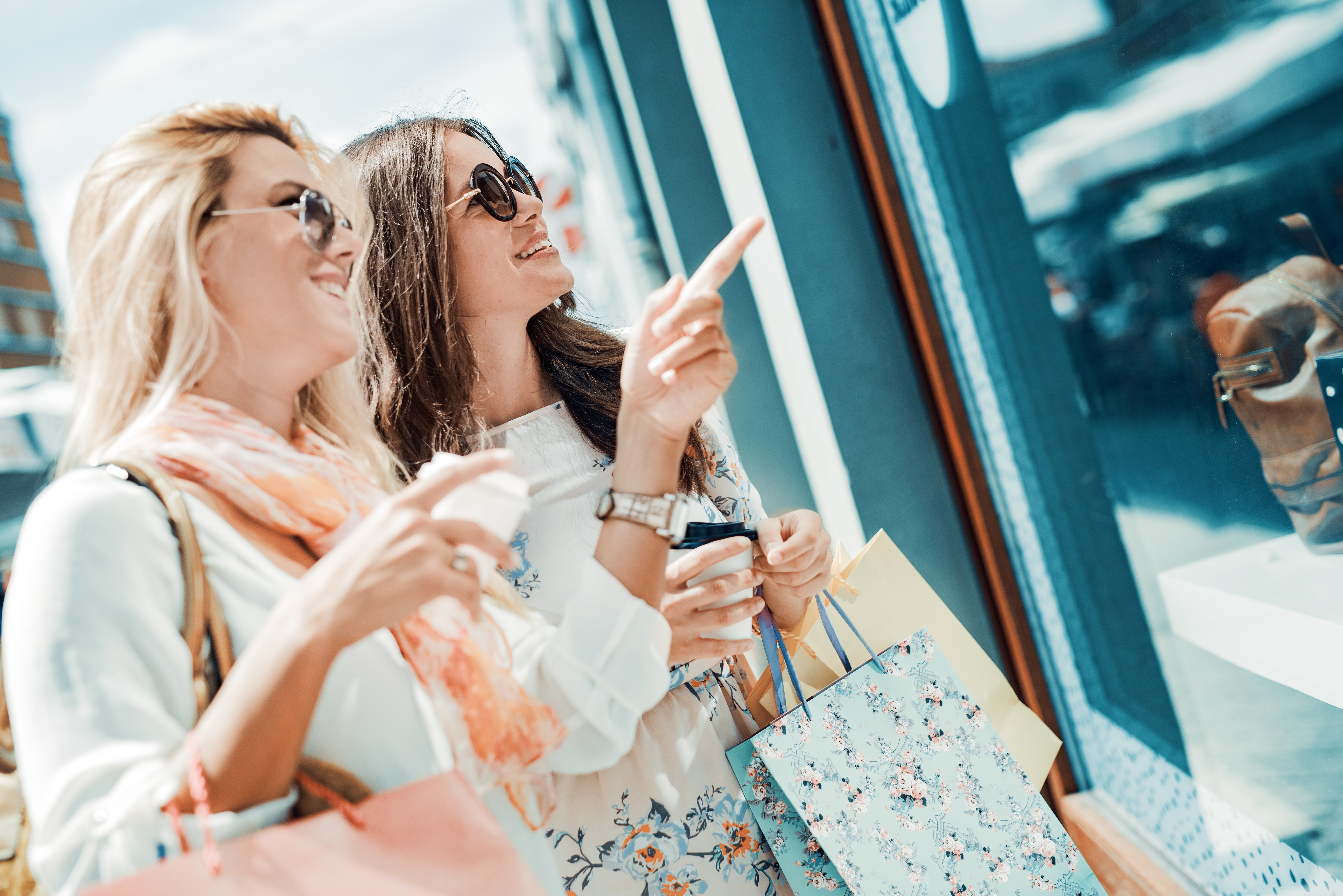 Happy woman with shopping bags pointing finger in the shop window.