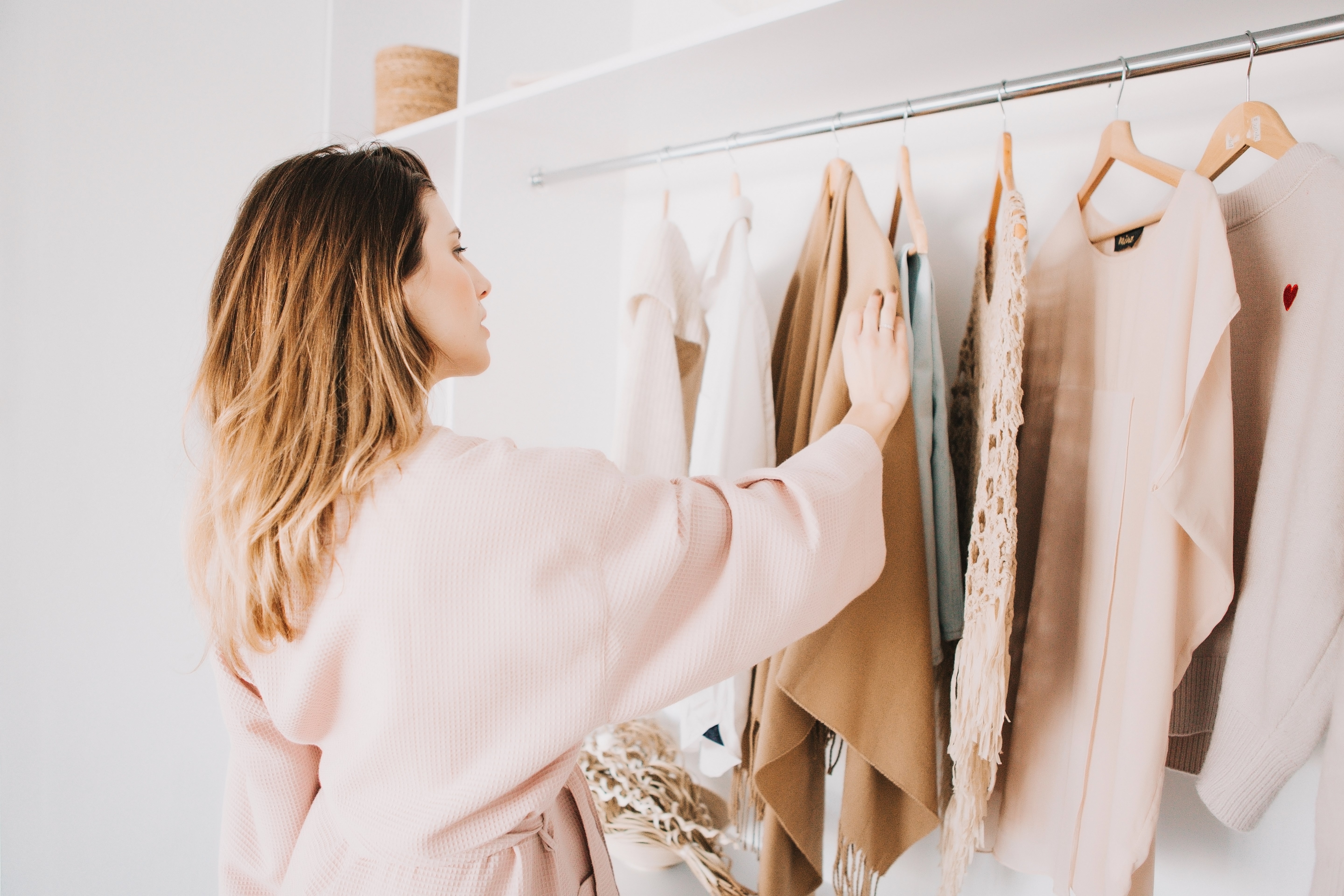 Young woman in bathrobe standing in front of hanger rack and trying to choose outfit dressing for work or walk.