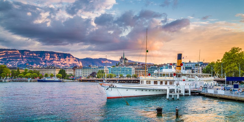 Panoramic view of the historic city center of Geneva with traditional paddle steamer boat on Lake Geneva in beautiful golden evening light at sunset with blue sky and clouds in summer, Switzerland