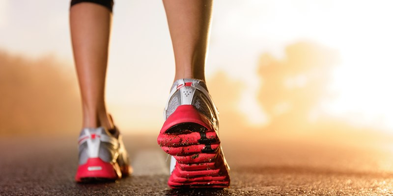 Runner feet running on road closeup on shoe. woman fitness sunrise jog workout welness concept.