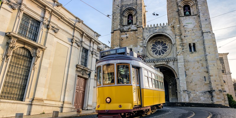 A famous yellow tram 28 passing in front of Santa Maria cathedral in Lisbon, Portugal