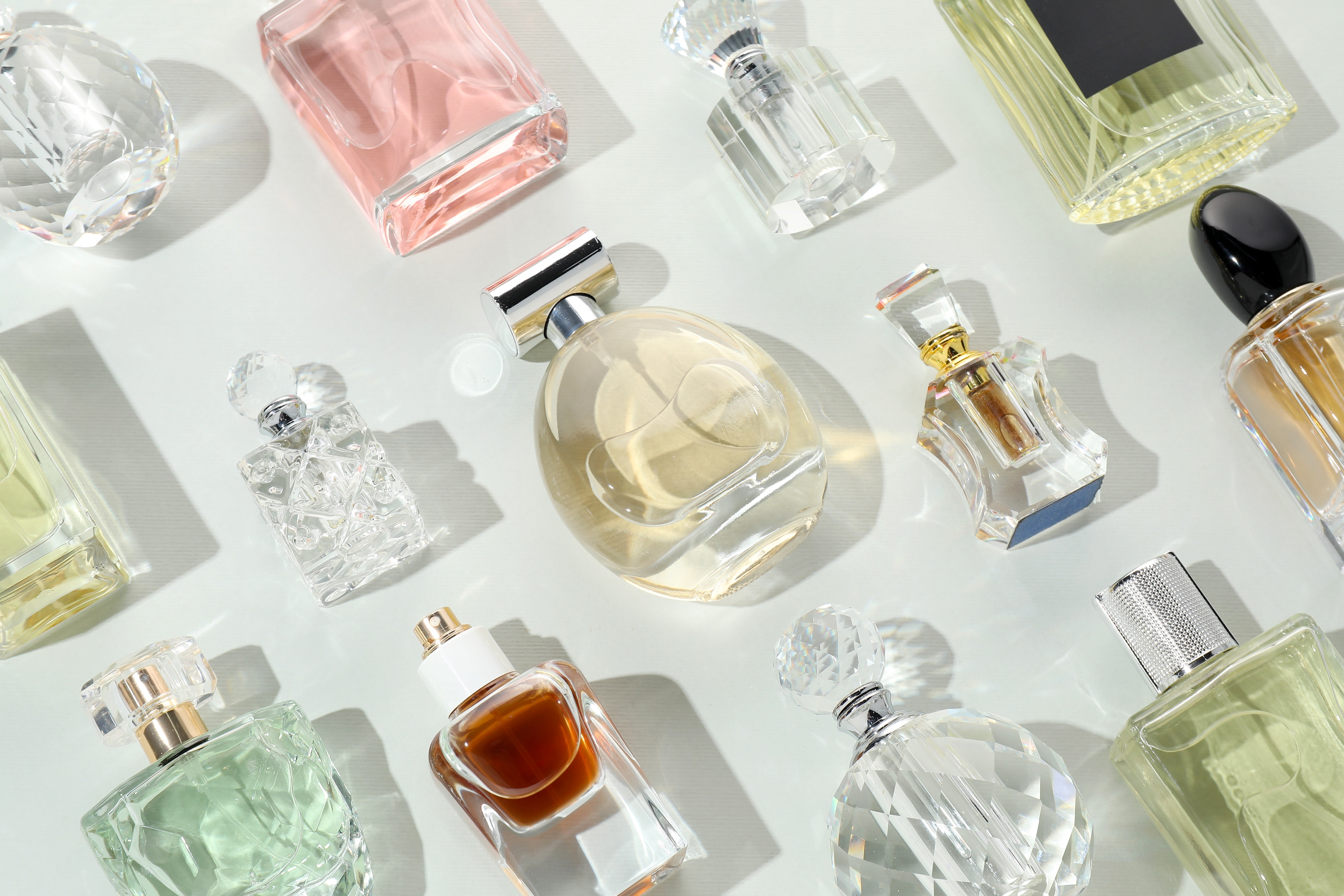 Bottles of various perfumes on light background, flat lay