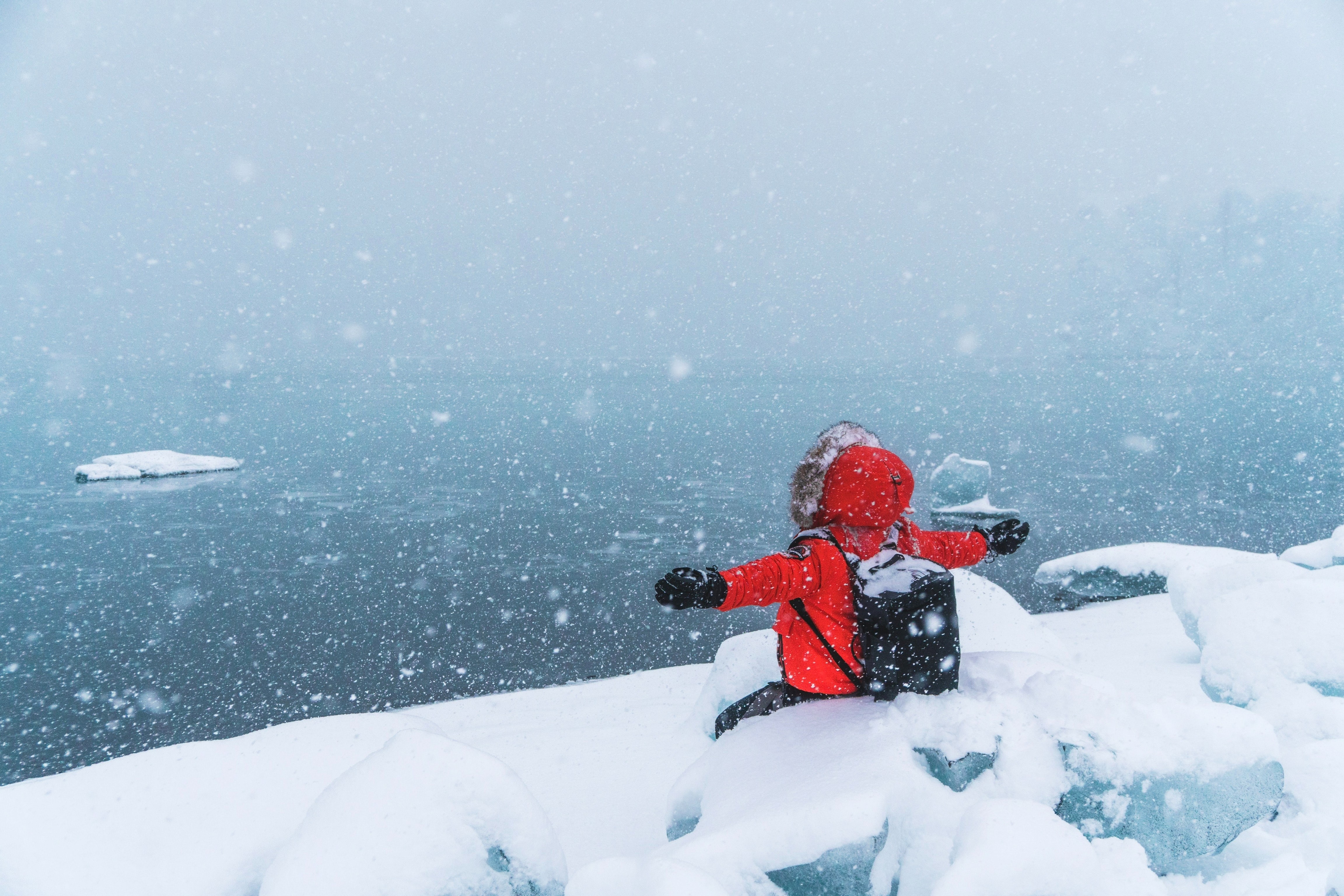 person in red jacket next to a glacier lake