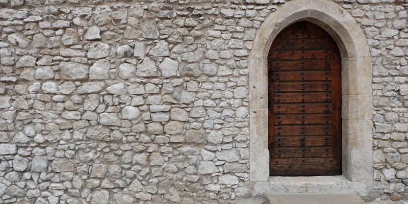 Heavy closed door on a stone wall of a medieval fortress, made of riveted wood