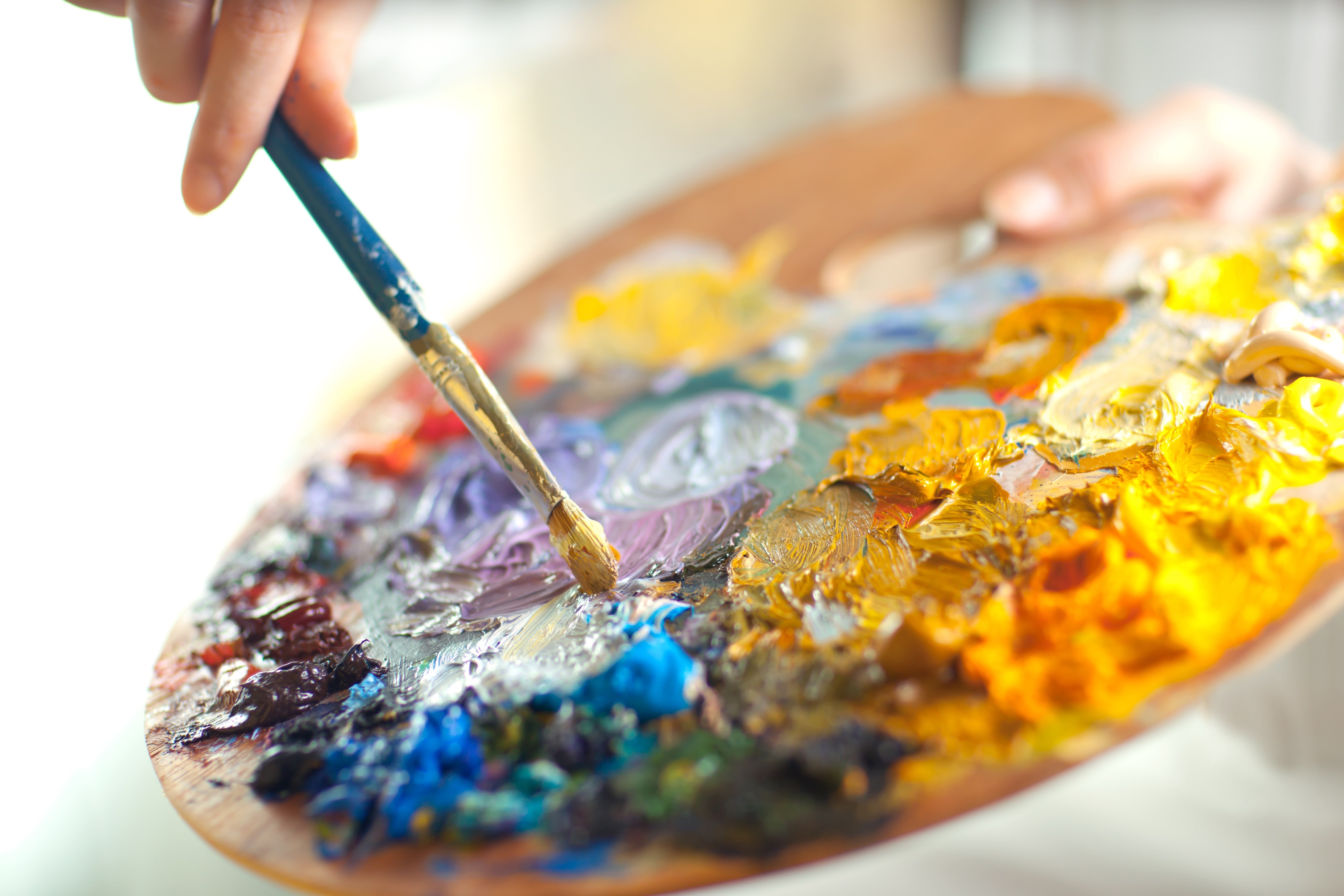 artist brush mix color oil painting on palette is holding in his hand closeup