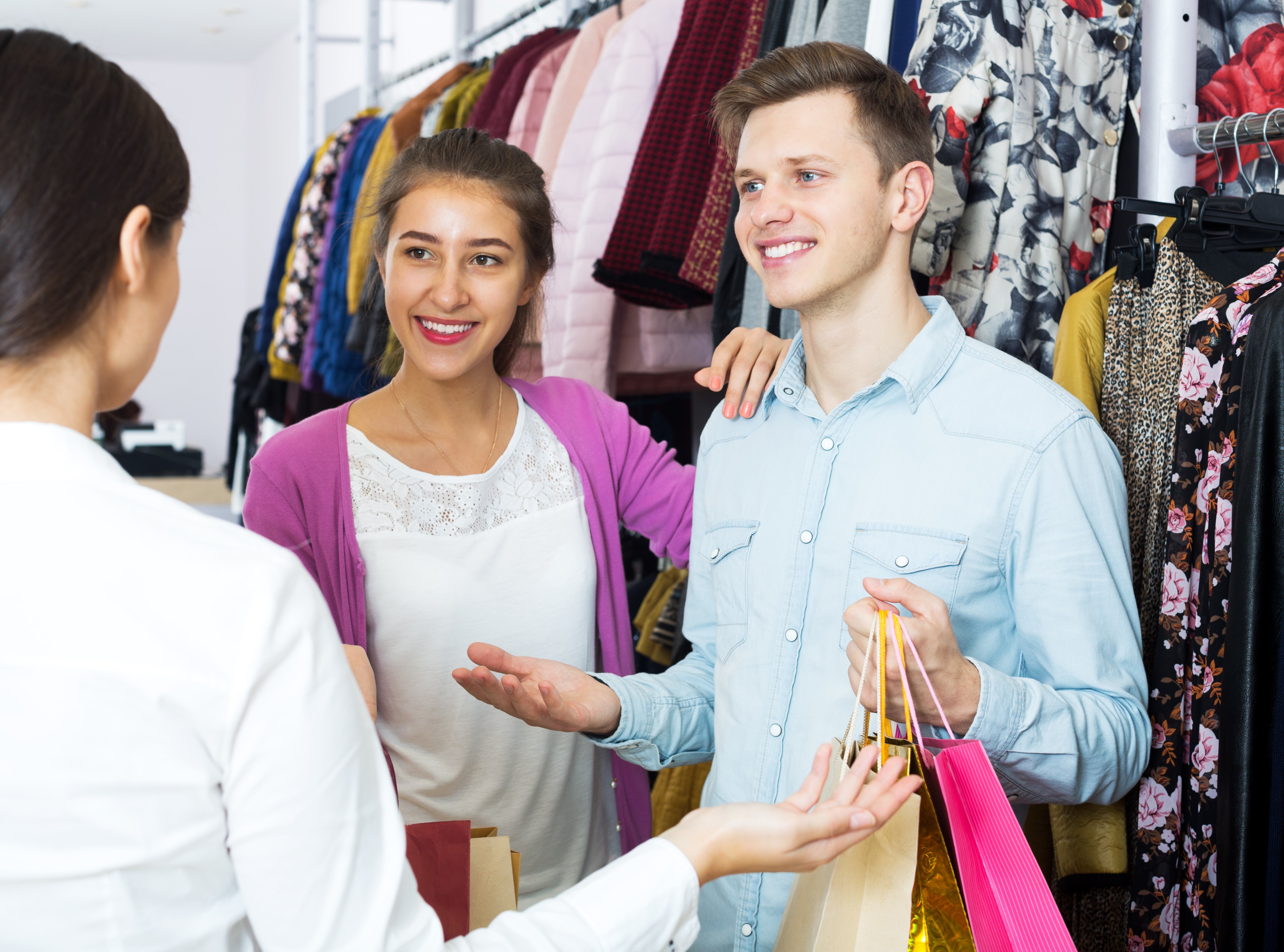 Female assistant serving happy couple customers asking in clothing boutique