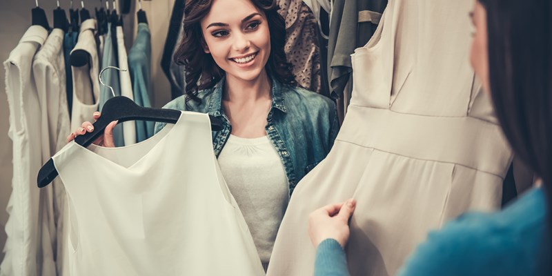 Beautiful girls are choosing clothes, talking and smiling while doing shopping in boutique