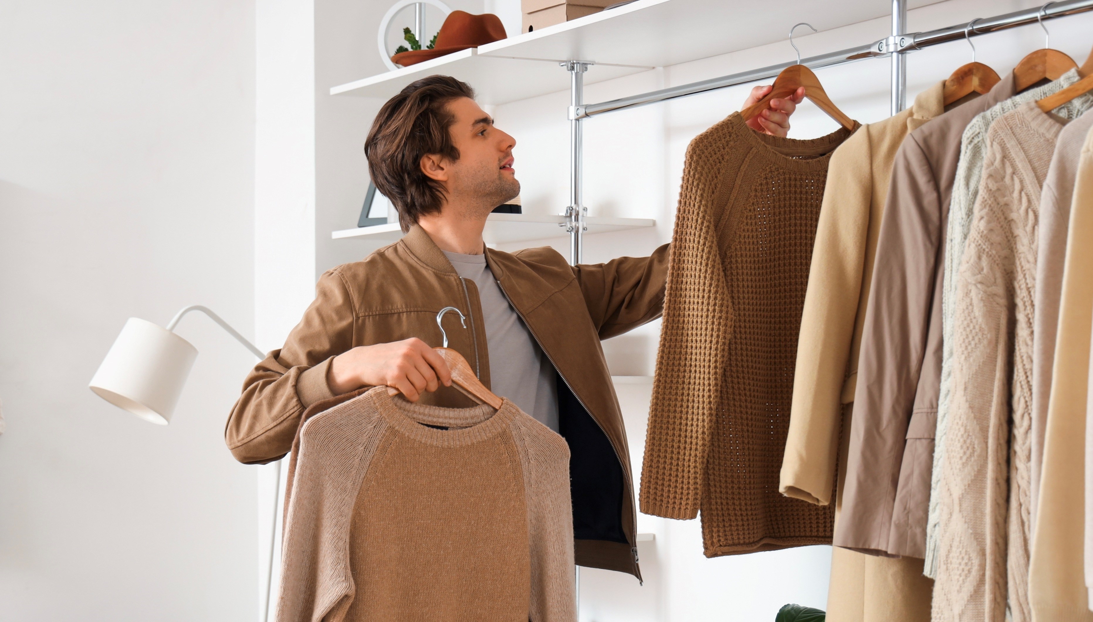 Handsome young man arranging stylish clothes in dressing room