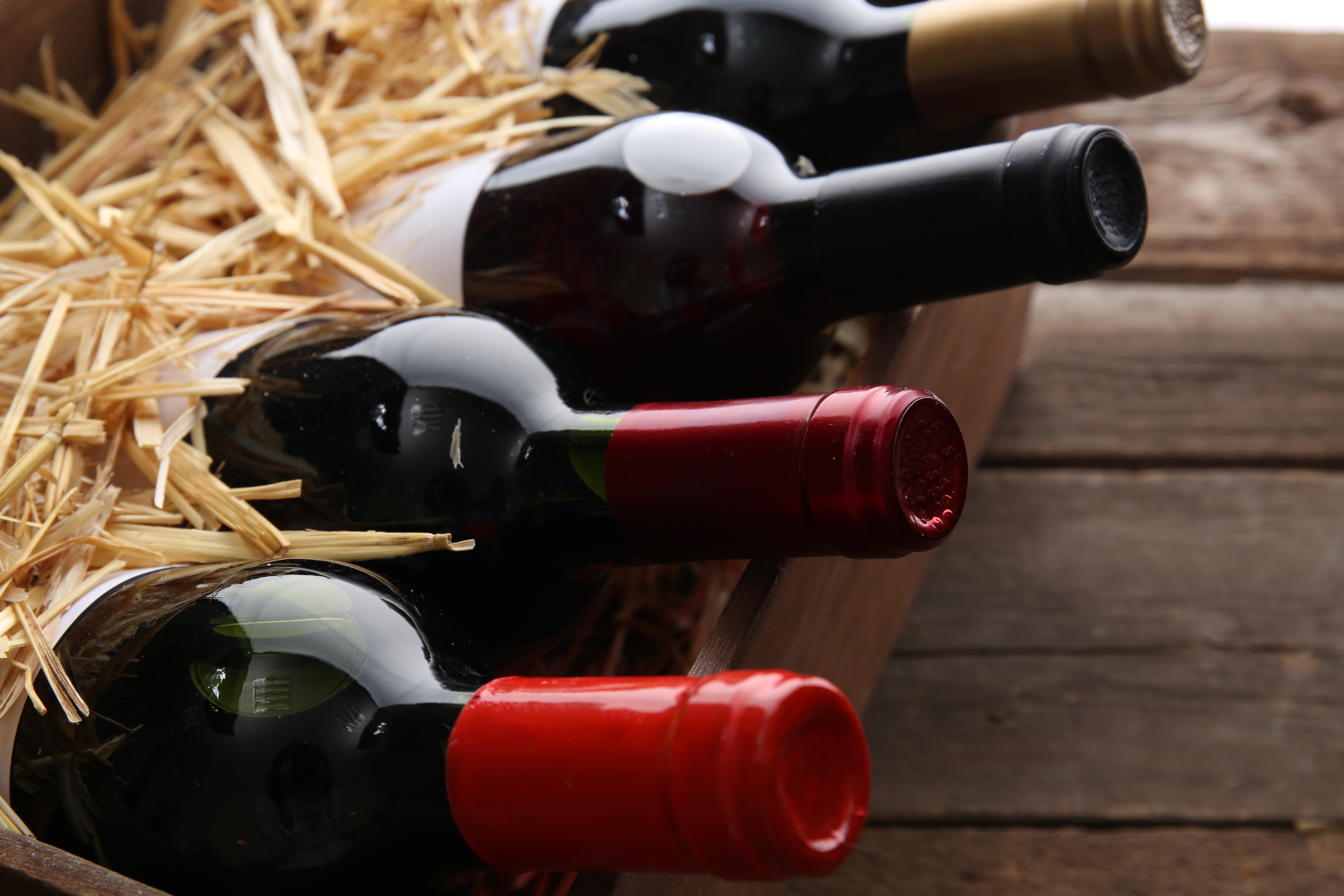 Box with straw and wine bottles on wooden background
