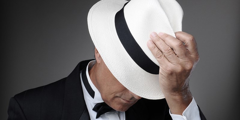 Closeup of a middle aged man wearing a tuxedo and a Panama Hat. Horizontal over a gray background.