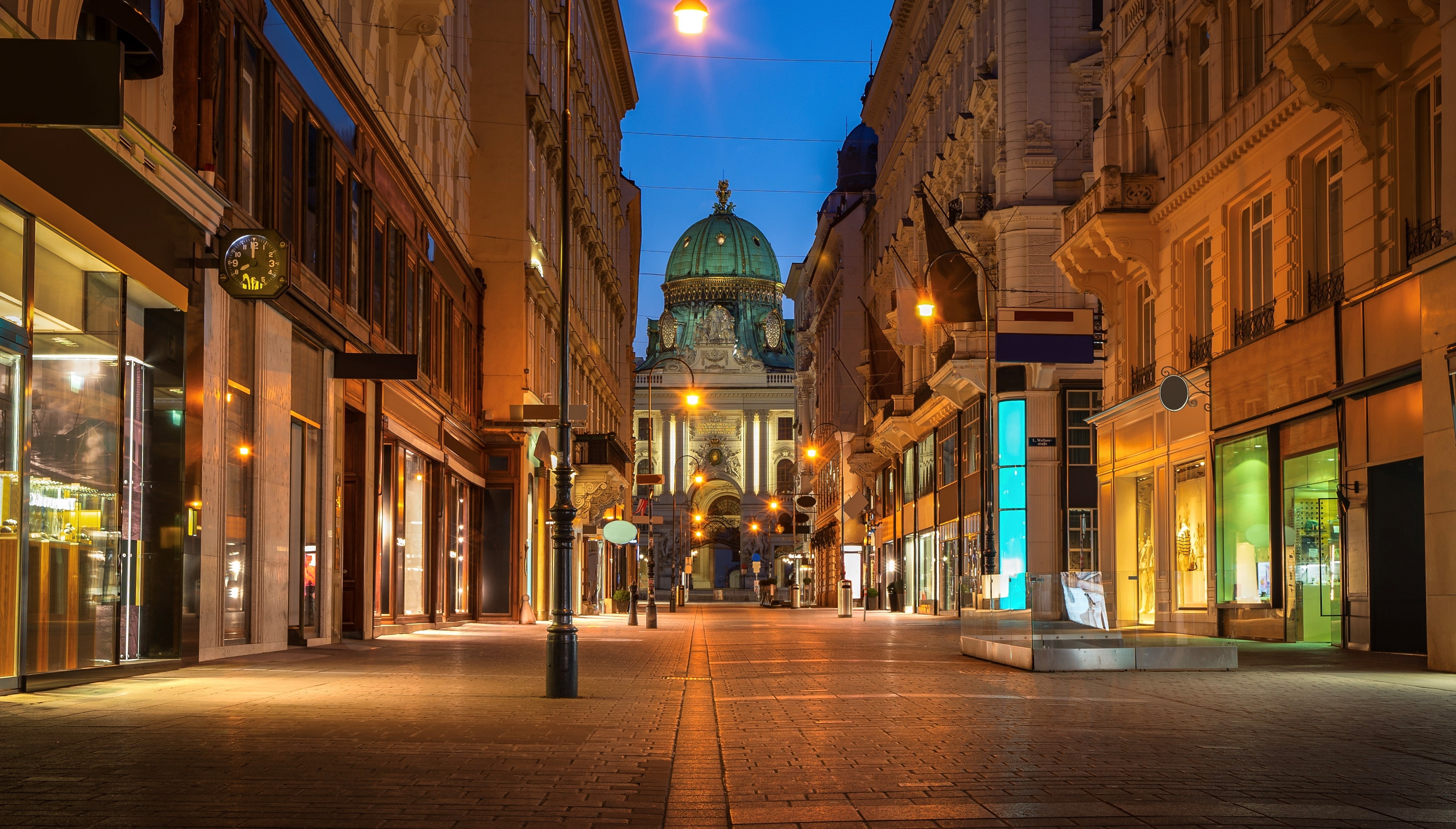 Shopping street in Vienna (Kolhmarkt) leading to historical palace Hofburg during evening with street lights