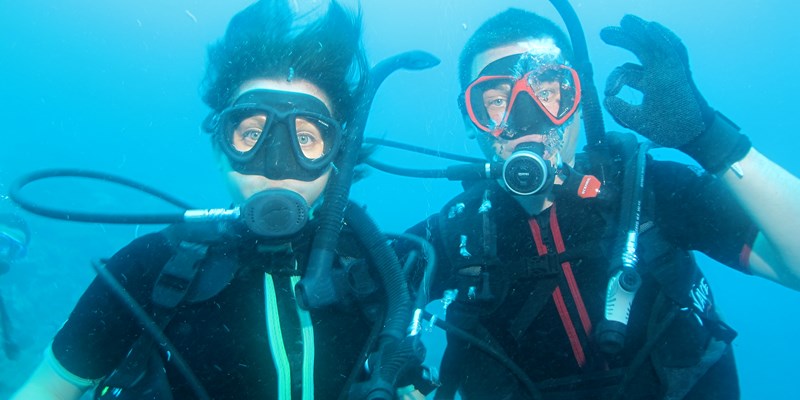 two divers underwater, one showing the OK sign