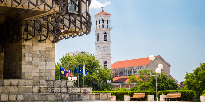 En kyrka och en stenbyggnad bredvid flaggstänger i Pristina En kyrka och en stenbyggnad bredvid flaggstänger i Pristina