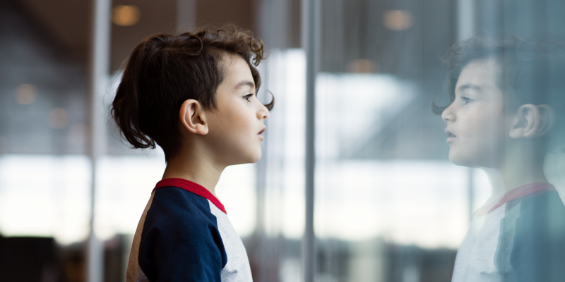 A child is looking through the window. The child mirror image is visible on the window. A child is looking through the window. The child mirror image is visible on the window.