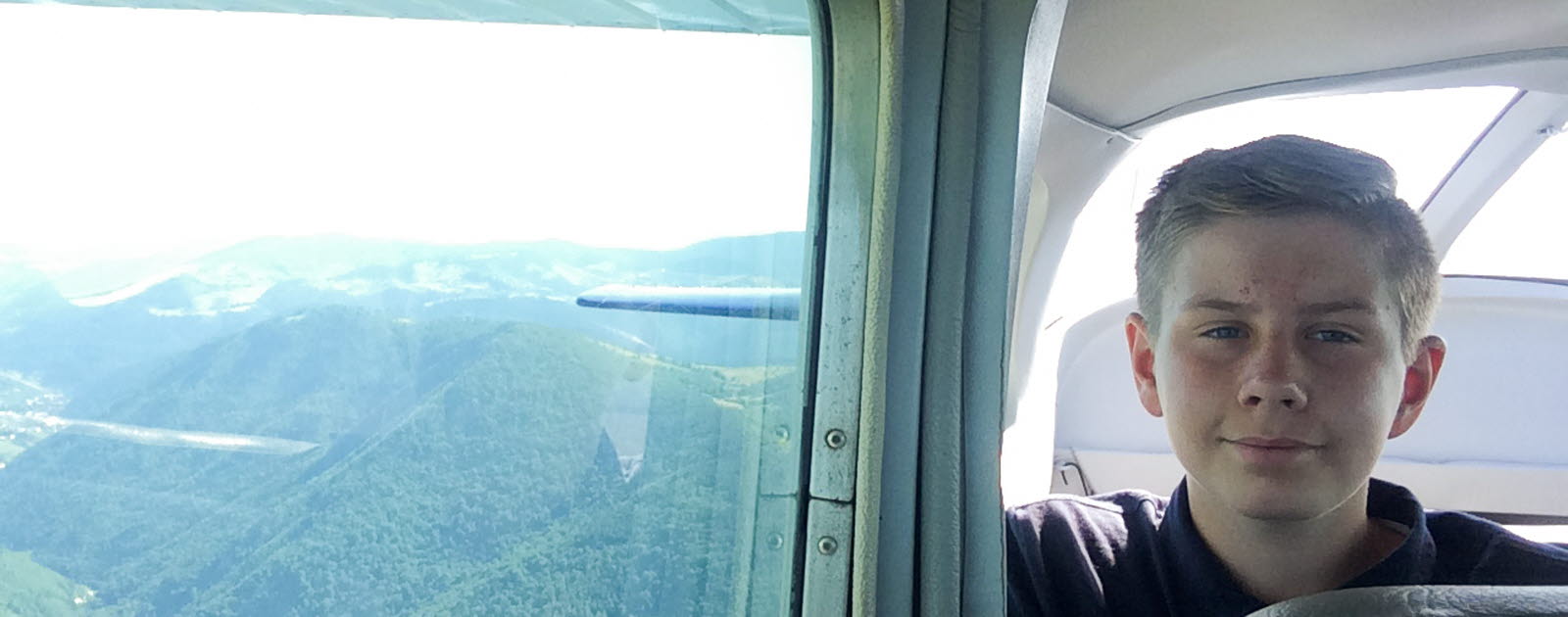 Pojke tittar ut från flygplan på grönklädda berg Pojke tittar ut från flygplan på grönklädda berg