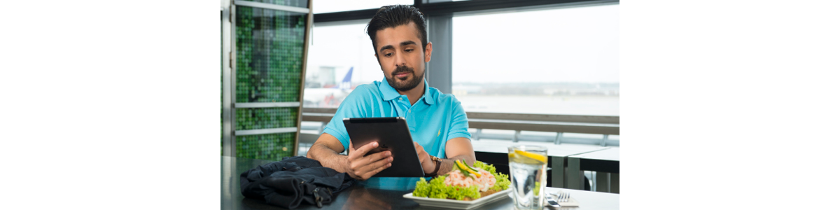 En man vid ett bord hållandes en tablet med en räksmörgås framför sig En man vid ett bord hållandes en tablet med en räksmörgås framför sig