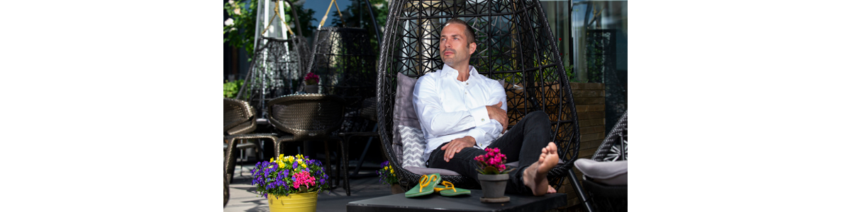 En man i en hängande stol, ena foten på bordet och ett par flipflops bredvis En man i en hängande stol, ena foten på bordet och ett par flipflops bredvis