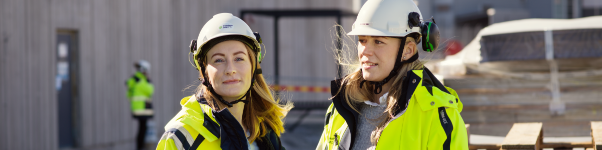 Två kvinnor med bygghjälmar och varseljackor på en byggarbetsplats Två kvinnor med bygghjälmar och varseljackor på en byggarbetsplats